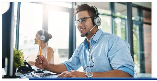 Ein Mitarbeiter sitzt vor seinem Computer und telefoniert mit seinem Headset über einen VoIP Telefonanlage.